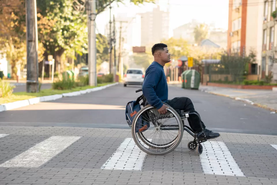 Young man in wheelchair crossing zebra crosswalk.